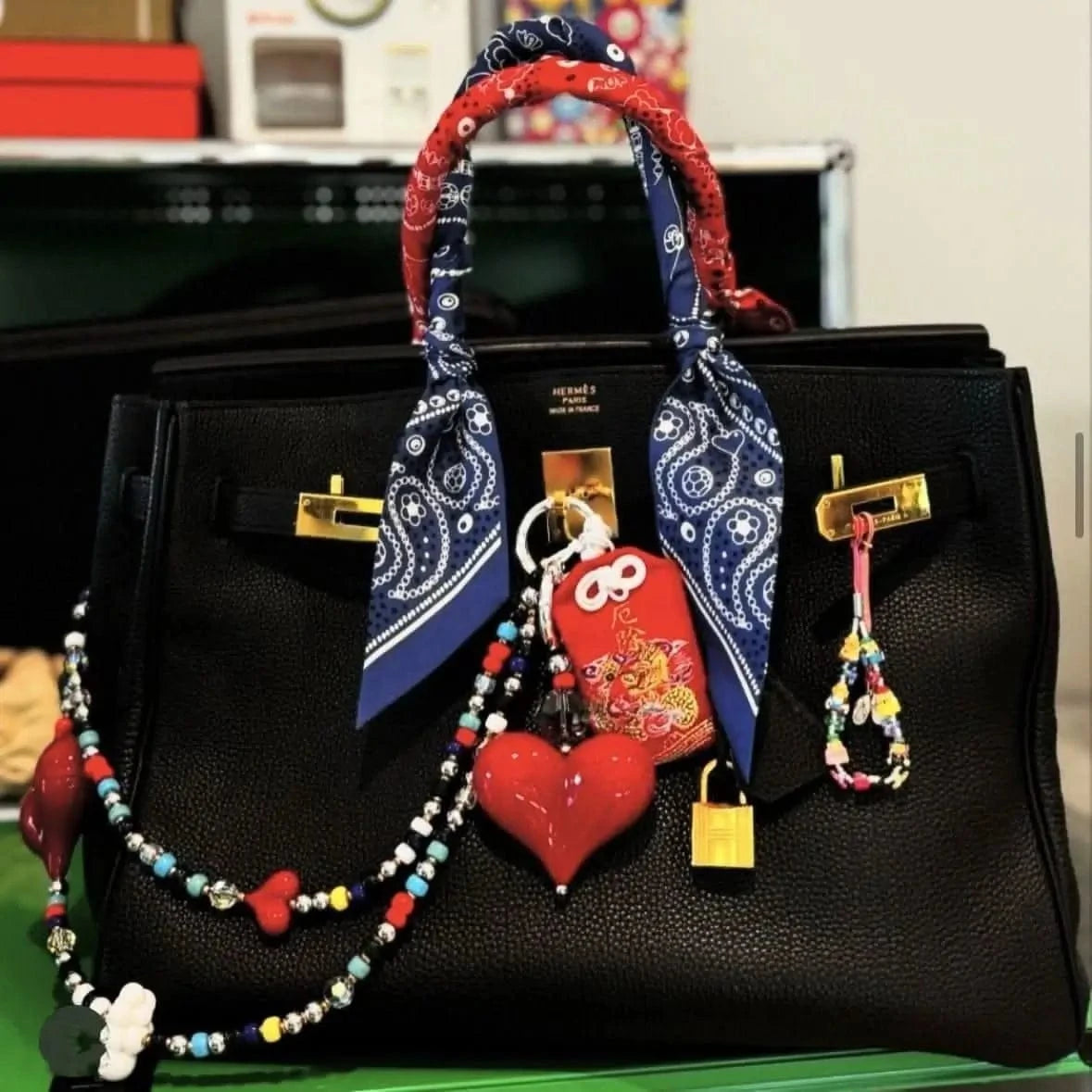 Bead Parade red silk twilly scarf elegantly tied around the handle of a luxury handbag, adding a vibrant and playful accent.