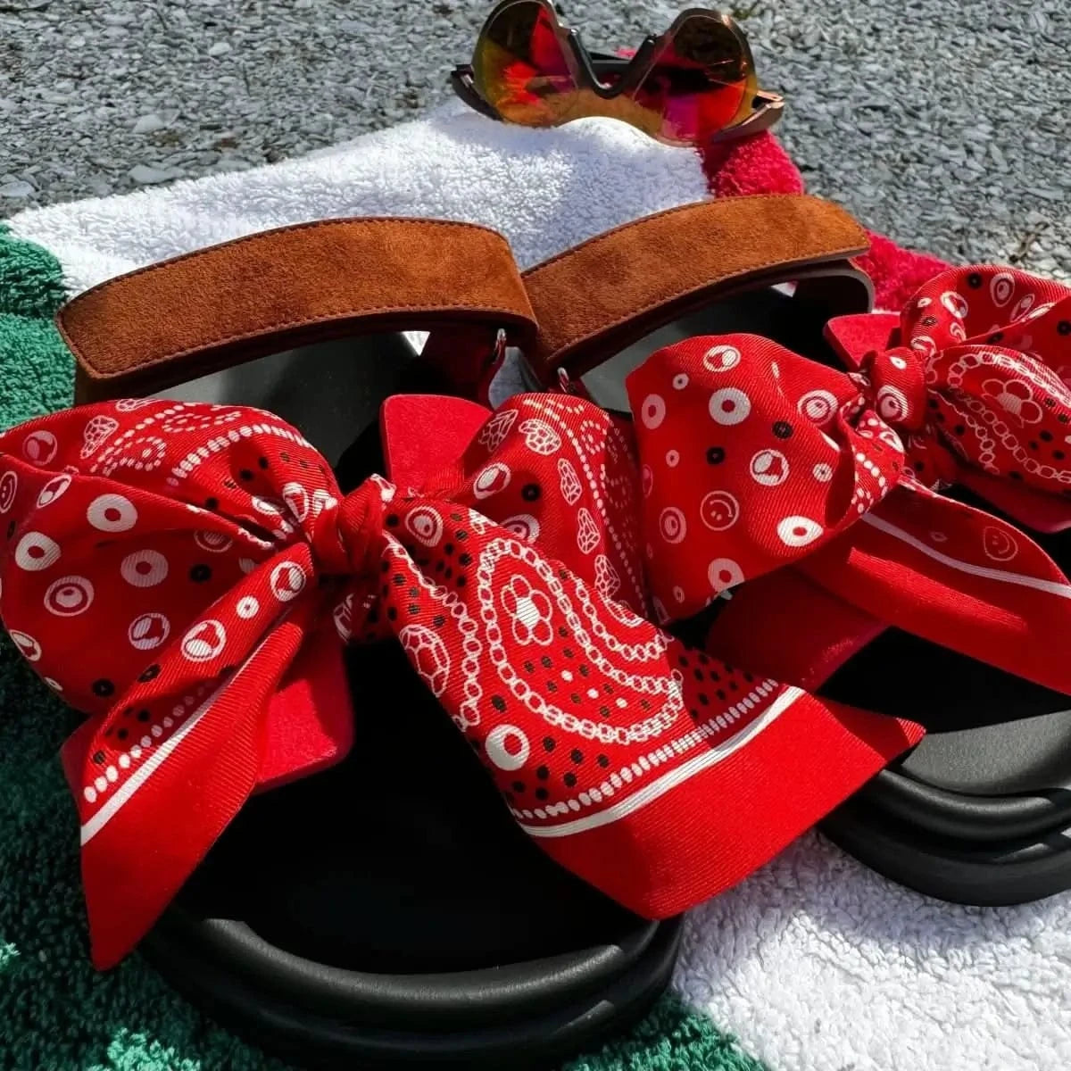 Close-up of the red Bead Parade silk twilly scarf styled as a decorative bow on a pair of luxury shoes, highlighting its intricate bead-inspired pattern.