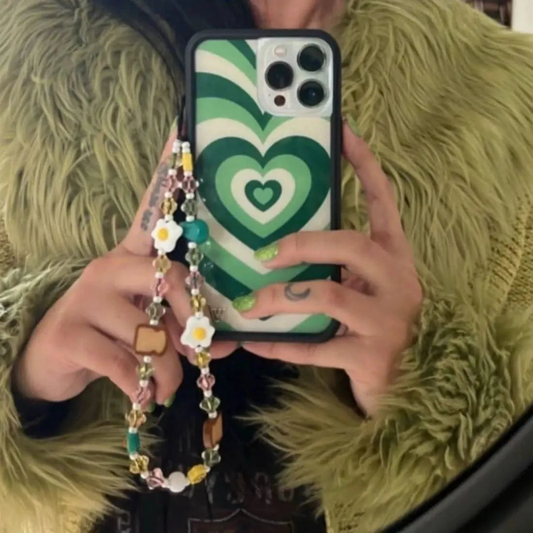 Mirror selfie of a person holding their phone with the Breakfast Club Wristlet Phone Strap visible, featuring playful breakfast-themed beads dangling from the case.
