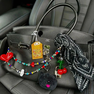 Black Bead Parade bandana tied stylishly around the handle of a designer handbag, adding a chic and colourful accent.