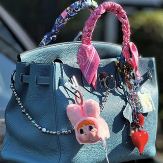 Bead Parade pink silk twilly scarf tied around the handle of a designer handbag, adding a vibrant and playful accent.