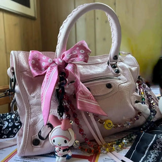 Close-up of the pink Bead Parade silk twilly scarf styled as a decorative bow on a luxury purse, highlighting its intricate bead-inspired pattern.