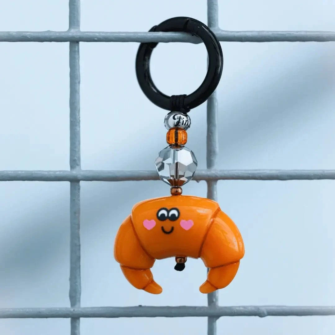 The Breakfast in Paris Bag Charm dangling from a wire gate, with the beads and crystal catching the sunlight, creating a cheerful and whimsical effect.