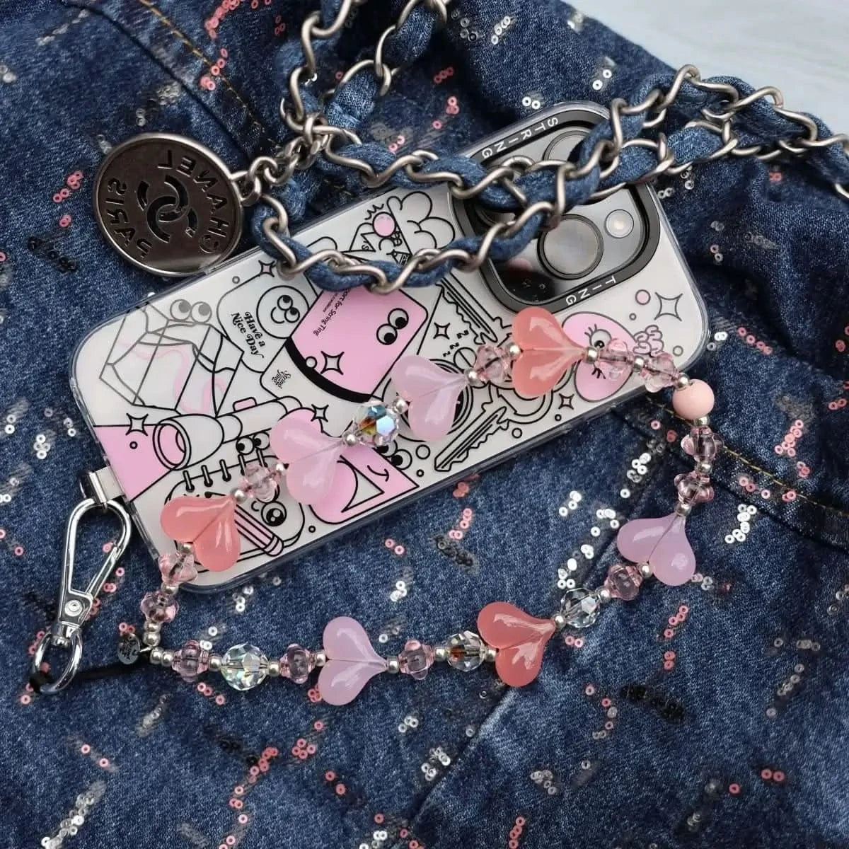 Smartphone with a String Ting case placed on a denim surface, adorned with the Cherry Blossom Kawaii Wristlet Phone Strap, showcasing its delicate pink beads and heart accents.