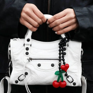 Close-up of a Balenciaga handbag adorned with the Cherry Drop Obsidian Bag Charm by String Ting, showcasing the charm's playful cherry design and elegant obsidian beads.